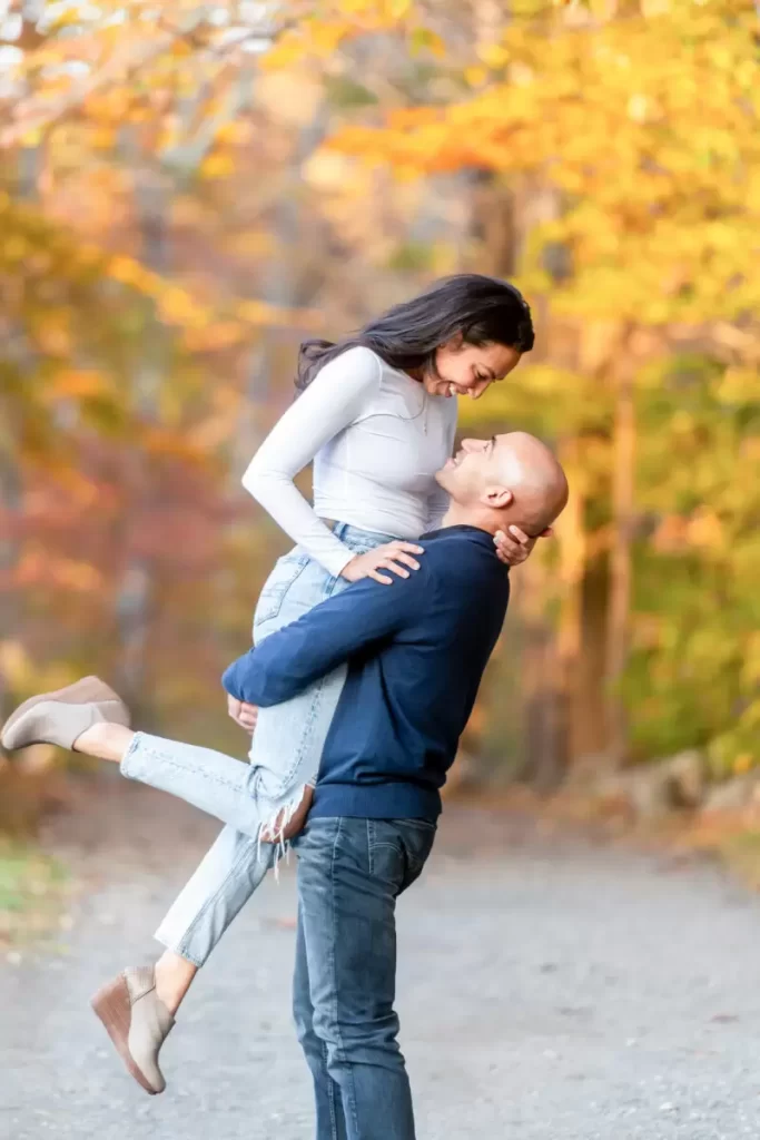 man picking up woman outdoors amongst fall foliage for an engagement photoshoot 