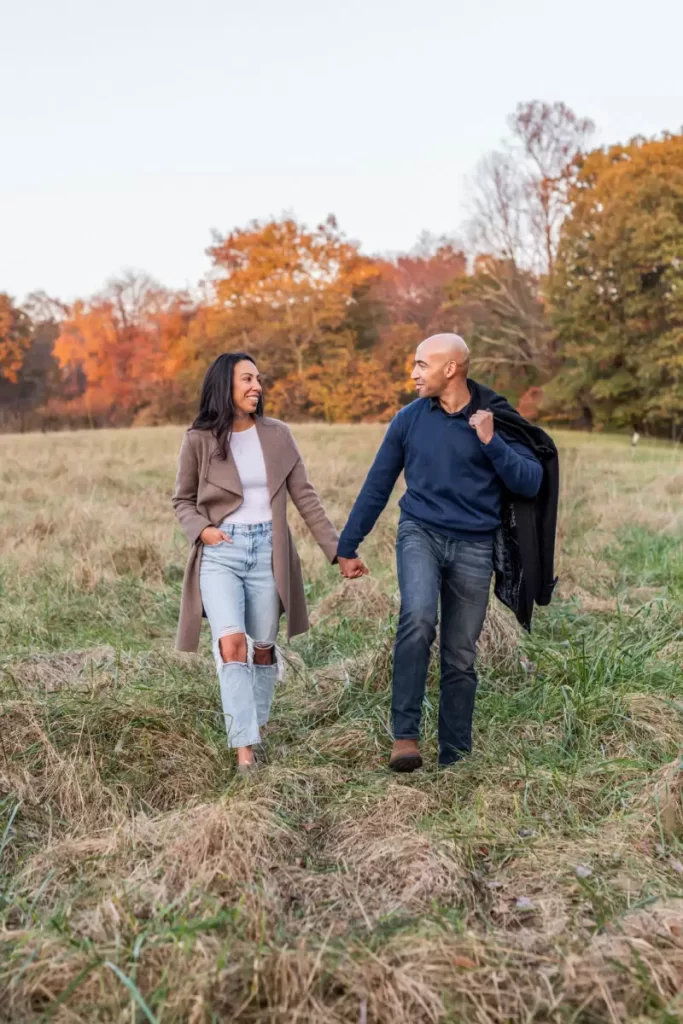 couple walking through field in autumn holding hands for engagement photoshoot